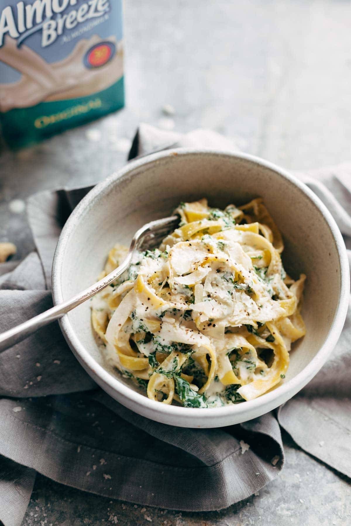 Pasta in a bowl with a fork and almond breeze in the background.