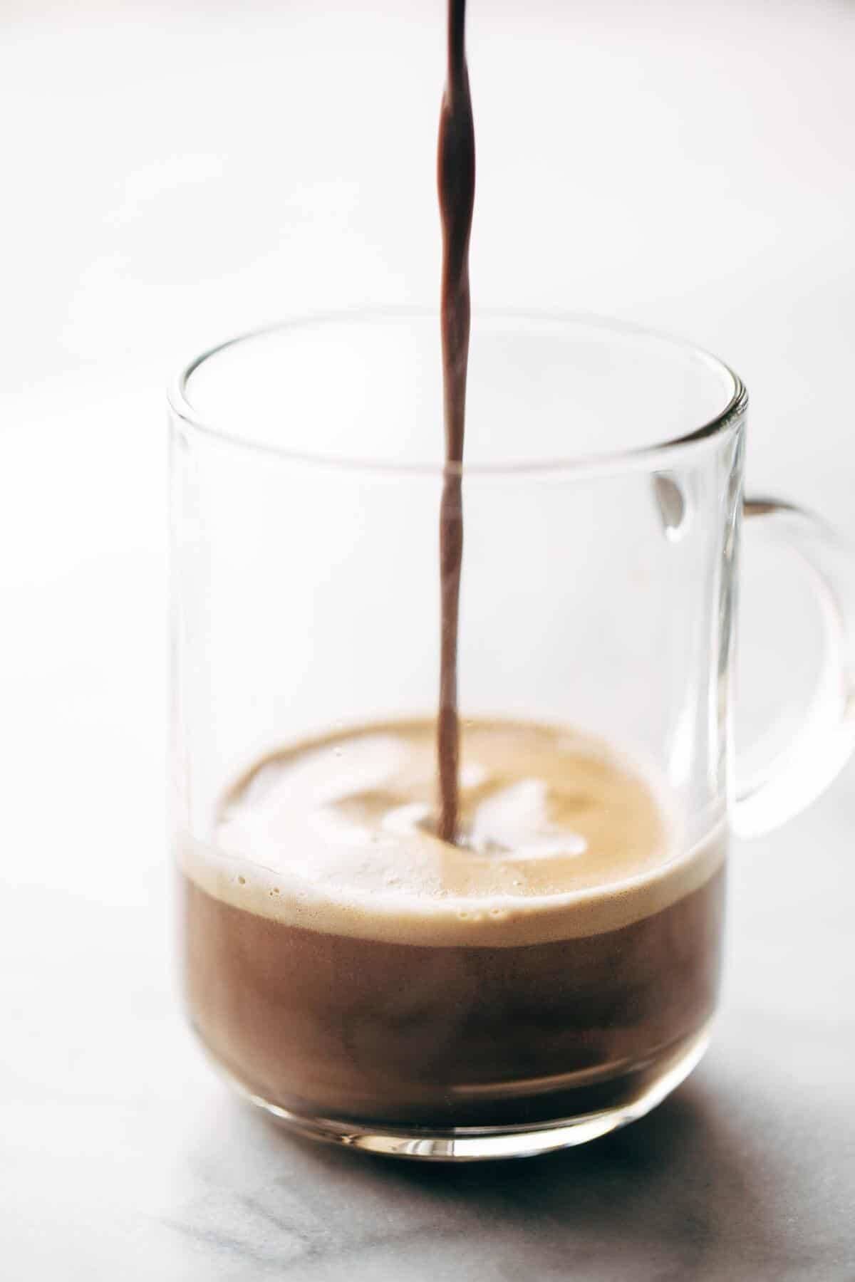 Clear glass with mocha being poured inside.