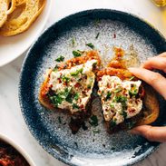 White hand grabbing Zaalouk toast on a plate